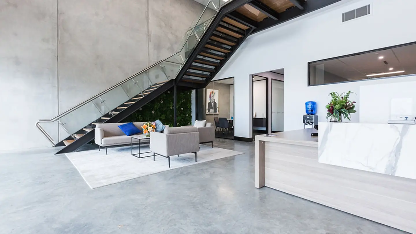 An office reception with a timber staircase, a lounge and a stone counter